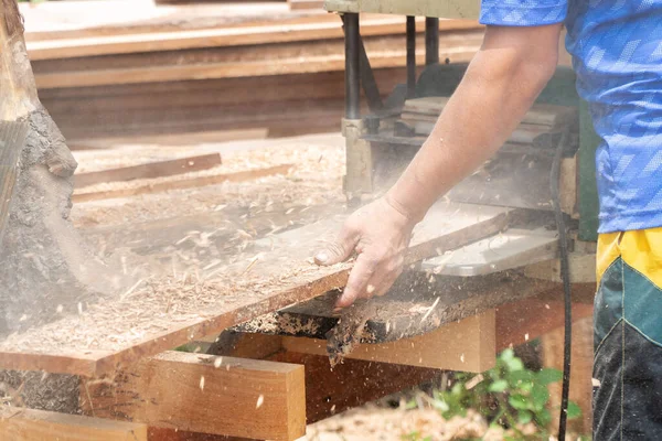 stock image Joiner, Man's hand scouring a wooden board on a thickness machine in garden. Carpenter working with electric planer on wooden beam, plank.DIY concept