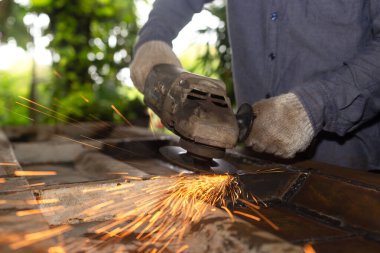 Heavy Industry Engineering Factory Interior with Industrial Worker Using Angle Grinder and Cutting a Metal Tube. Güvenlik Üniforması ve Sert Şapka Üretim Metal Yapıları Müteahhiti.