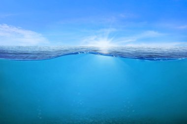 Suyun altındaki mavi dalgalar ve kabarcıklar. Sakin denizin üzerindeki güzel beyaz bulutlar güneş ışığı yansıması, sakin su yüzeyinin sakin deniz uyumu. Güneşli gökyüzü ve durgun mavi okyanus. 