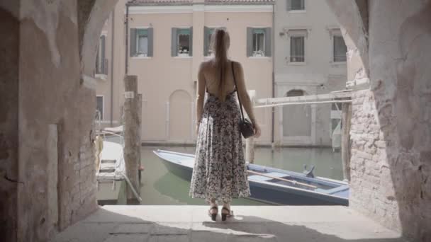後ろから立っている女性はベネチアン運河の水の上のボートを見て — ストック動画