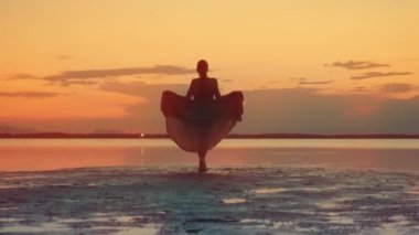 Model gölün kızıl günbatımında boyalı suda yürüyor.