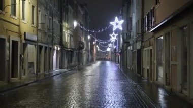 Street with brick pavement at night, slightly wet from rain, reflecting the christmas lights hanging above.