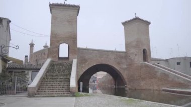 Ancient bridge of the city in Emilia-Romagna, placed over a water channel. The bridge has two entrances with brick stairs and two towers on the sides. 