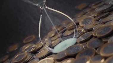 Sand falls into hourglass on the table around which many euro coins are scattered