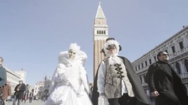 Venice, Italy - February 2023. Two women with beautiful ancient royal masks in front of the Venetian high tower at the Carnival
