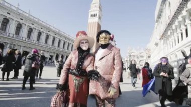 Venice, Italy - February 2023. Elegant couple with masks in Venice and in front of San Marco tower