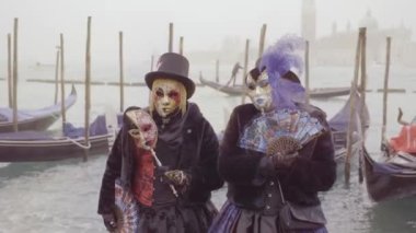 Venice, Italy - February 2023 - Masks stopped in front of gondolas at the carnival in the fog