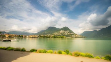 Lugano Gölü 'nün önündeki yeşil dağların manzarası ve zaman ayarlı gökyüzü.