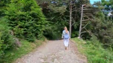  Bir kadın, resimli dağ ormanlarıyla çevrili toprak bir yolda güvenle yürür. Yolu geçerken, doğanın taşıdığı huzurlu ve huzurlu atmosferi hissedebiliyor..