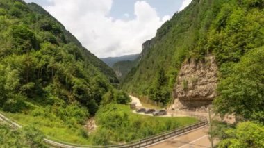 Dağlarda yeşil ağaçlarla kaplı dağlar ve yoldan geçen arabalar.