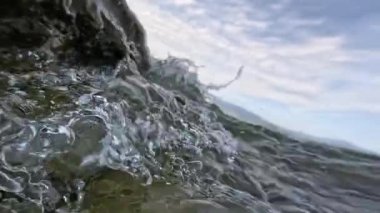 Kayalar, taşlar ve deniz dalgaları arasında kameranın hareketi. Kamera suyun üstünde ve altında yavaş çekimde çeker..