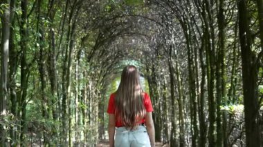 Genç bir kadın ince ağaçların yaptığı tünelin altından geçiyor.