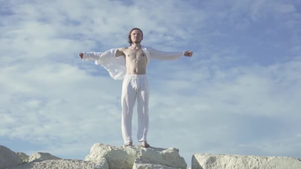 青い空の背後にある石の上に立って 長い髪の白い服を着た男 — ストック動画
