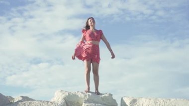 Genç bir kadın kollarını rüzgara, kayalara ve çıplak ayaklara açmış mutlu bir şekilde ayakta duruyor..