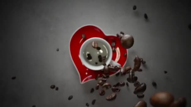コーヒー豆は 上からカップの外に出て テーブルの上に小さな赤いハート型のプレートに落ちる 上からのマクロショット — ストック動画