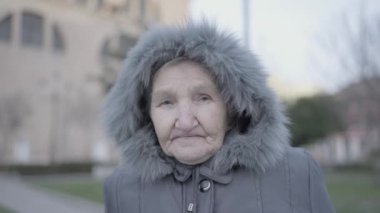 Kürk parka ceketli yaşlı bir kadın bir binanın önünde duruyor, yüzü tüylü kaputtan dışarı bakıyor. Dondurucu hava onun eğlencesini engellemiyor.