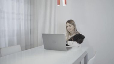Bir kadın dizüstü bilgisayarı ve köpeği kollarında bir masada oturuyor. İçerisi açık gri tonlarda tasarlanmış. Hoş bir atmosfer yaratıyor..