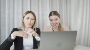İki kadın zarif ve profesyonelce giyinmiş, dizüstü bilgisayarla konuşuyor, bir şeyler tartışıyor ve gülümsüyor.