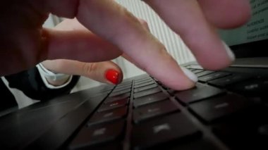 Parlak kırmızı tırnaklı bir kadın dizüstü bilgisayarda daktilo kullanıyor. Hassas ve hızlı. Parmakları uzman jestleriyle tuşlara vuruyor.