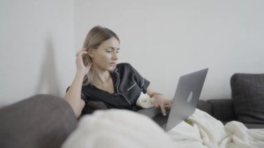 Bir kadın rahat bir şekilde kanepede dizüstü bilgisayar kullanarak oturuyor, parmaklarını klavyeye basıyor..
