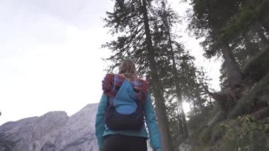 Sırt çantalı kadın orman ağaçlarının ve dağların altında yürüyor.