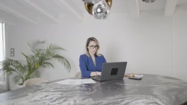 Evde ya da ofiste masada oturan zarif bir kadın dizüstü bilgisayarla çalışıyor..