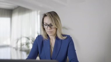 Zarif ve ciddi bir kadın, gözlük takıyor, evinde dizüstü bilgisayarına klavye takıyor..