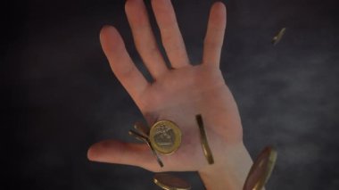 Bozuk paralar yukarıdan avucunun içine düşer ve siyah bir arka planda ellerini açar. Yukarıdan ateş edildi.