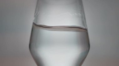 Bir makro çekim şeffaf bir bardağın içindeki suyu yakalar, hareketi ve sıvı dinamiğini yakından gösterir.. 
