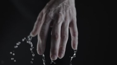 Su damlacıkları olan bir elin yakın plan görüntüsü, koyu bir arka plan üzerine kurulmuş, hem temizliği hem de nemi tasvir eder.