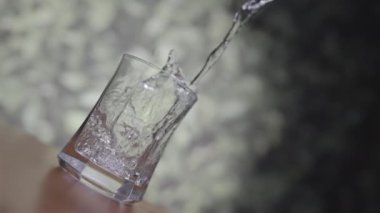 Kristal berraklığında, tatlı su şeffaf bir sürahiden kristal bir bardağa nazikçe dökülüyor, ve bu cam ince bir şekilde koyu ahşap bir masaya yerleştiriliyor..