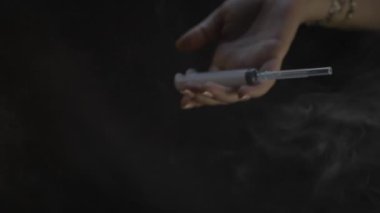 Karanlık bir ortamda, şırıngayı tutan bir el tıbbi bakımı temsil eder, karamsar ve dramatik bir görüntü yaratır.