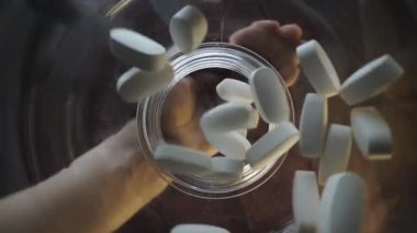 Video, soyut bir bakış açısıyla tasvir edilen beyaz hapları bırakmak için uzanan bir elin yakın çekimini gösteriyor.