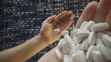 Bir el, mavi örülmüş arka planda birden fazla beyaz hap tutarken görülüyor, yakın plan çekimde çekiliyor.