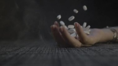 El yavaş çekimde masaya düşüyor ve avuç içinden beyaz haplar dökülüyor.