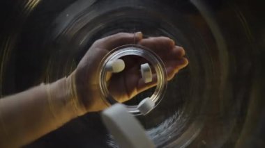 Resim, ilaç şişesini tutan, hapları ortaya çıkaran, ilaç ve sağlık hizmetlerini ön plana çıkaran bir eli yakalıyor.