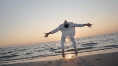 Arka planda büyüleyici güzellikteki günbatımında bir insan kumsalda neşeyle dans ediyor.