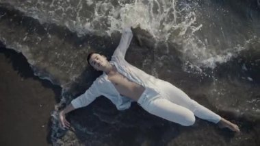 Huzur içinde uzanan bir insan sıcak, kumlu sahilde uzanır ve narin okyanus dalgalarıyla güzelce uyum sağlar.