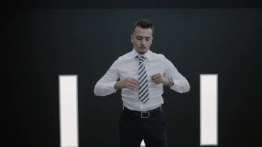 Kendine güvenen ve başarılı bir iş adamı şık bir takım elbise giymiş şık ve modern bir arka plana karşı kravatını düzeltiyor.