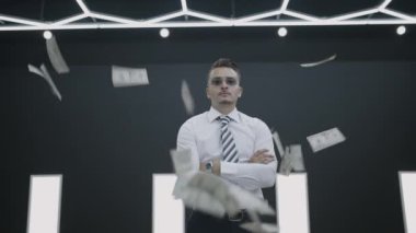 Kendine güvenen bir işadamı, etrafında para akarken dimdik ayakta duruyor, zenginlik kavramını mükemmel bir şekilde sembolize ediyor.