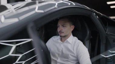 Bir adam şık ve şık spor arabaların içinde rahat bir şekilde otururken dikkatle odaklanır.