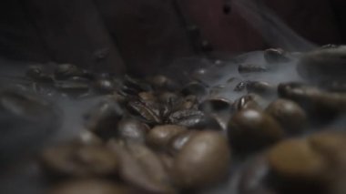 Taze kavrulmuş kahve çekirdeklerinin detaylı yakın plan görüntüsü. Havada aromatik buhar yükseliyor.