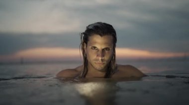 Güzel ve sakin bir gün batımı sahnesi, aşağıdaki huzurlu sularda süzülen yalnız bir yüzücüyü gösteriyor.