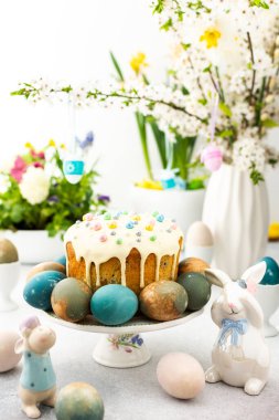 Paskalya Evi 'nin içi, vazonun arka planında yumurtalar, çiçek açan kiraz dalları ve buketler dolusu çiçekler, sevimli tavşanlar olan Paskalya pastası.