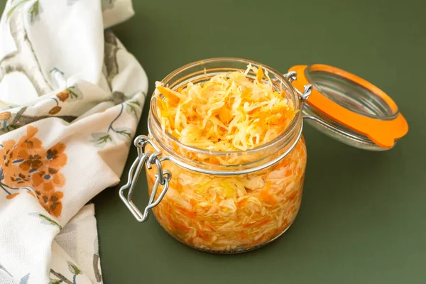 Fresh fermented vegetables, fermented cabbage with carrots in a glass jar on an olive background, healthy natural probiotics, healthy eating, sauerkraut