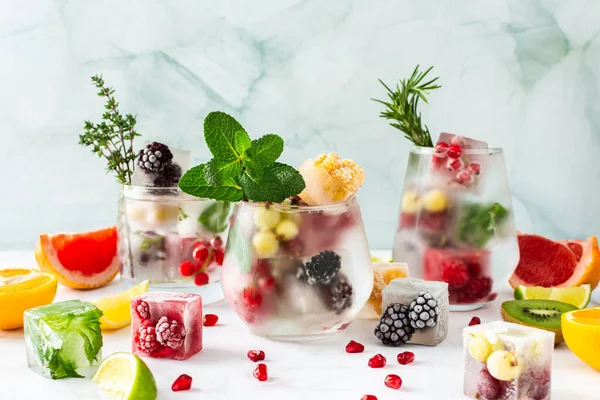 Refreshing drinks with ice cubes with fruits and citrus fruits, ice with blackberries and raspberries, gooseberries and currants, with mint, a jug of water and citrus fruits