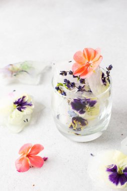 Refreshing cold drink with frozen flowers, colorful pansies and geraniums, lavender and Verbena