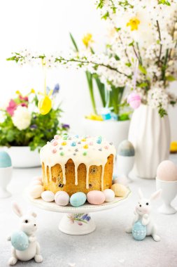 Paskalya Evi 'nin içi, vazonun arka planında yumurtalar, çiçek açan kiraz dalları ve buketler dolusu çiçekler, sevimli tavşanlar olan Paskalya pastası.