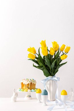 Şenlikli iç mekan, vazoda sarı laleler ve paskalya yumurtaları, sevimli tavşanlar ve Paskalya pastası.