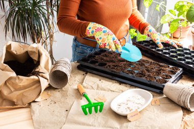 Domates tohumlarını plastik formlara ekme süreci ve turba çevre dostu formlar, toprak, mala ve tırmıkla dolu bir çanta, bahçeye iş ekme hazırlığı, bir kadın evde tohum ekiyor.